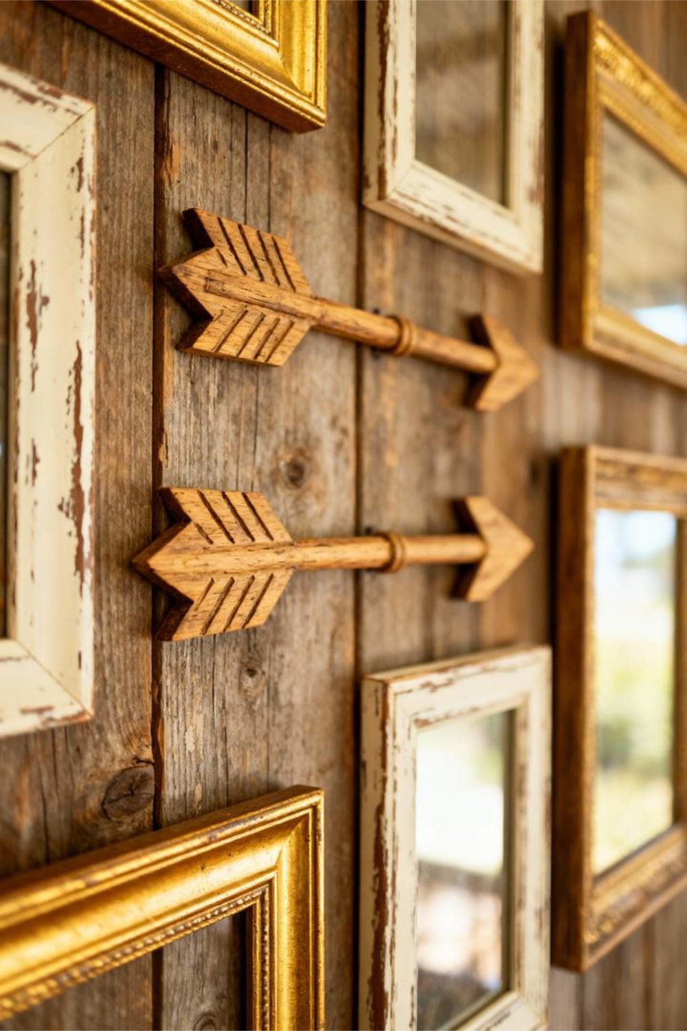 Close-up of rustic wooden decorative arrows styled on a farmhouse wall, mixed among frames for added movement.